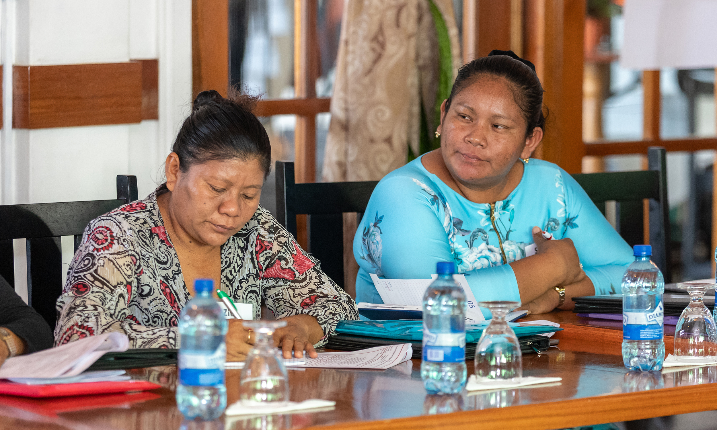 Two indigenous women leaders in Guyana sit at a table with papers and water bottles