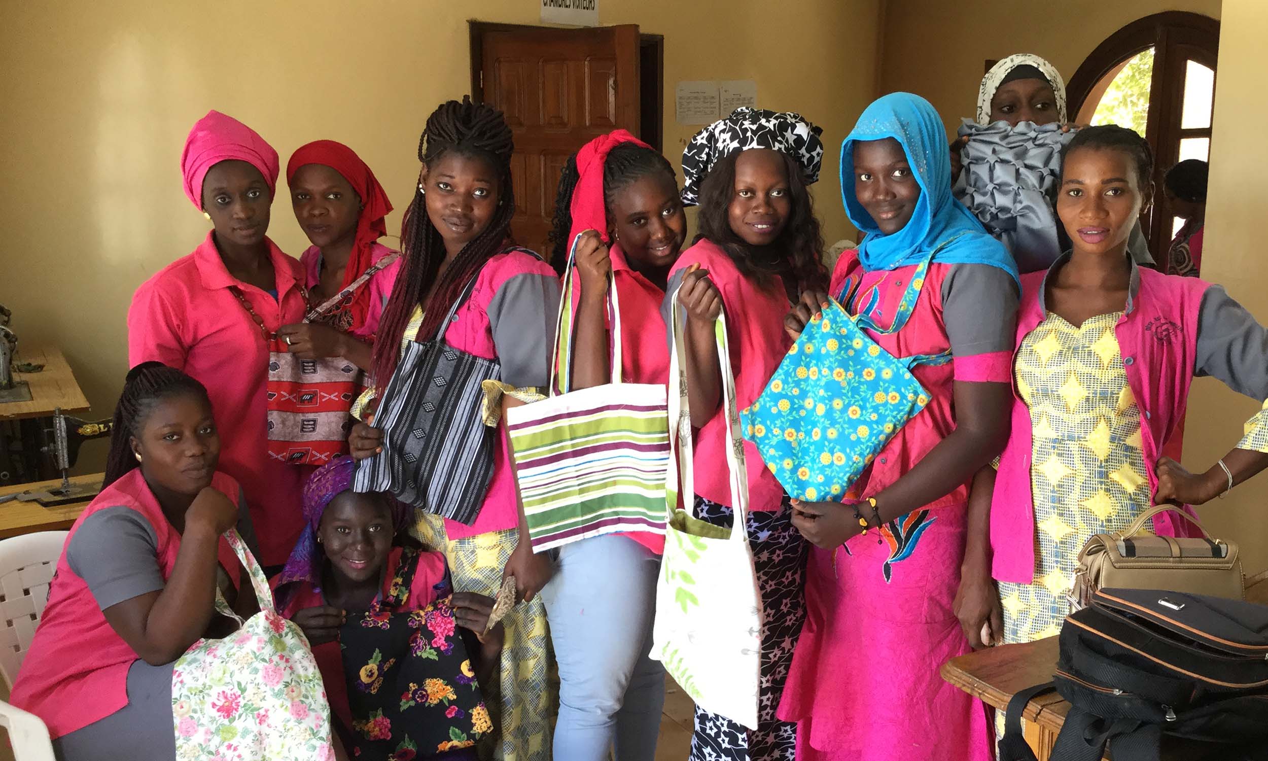A group of young Senegalese women hold up handcrafted bags