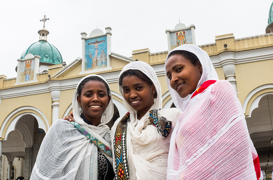Three young Ethiopian women put their arms around each other, standing outside an ornate building