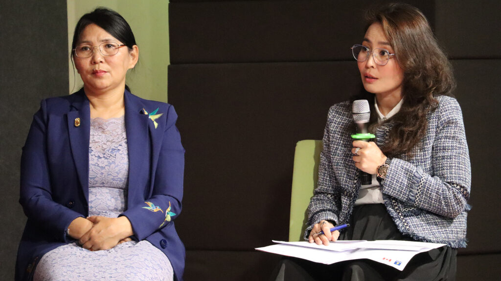 Two women working in governance in Mongolia seated beside each other, one holding a microphone