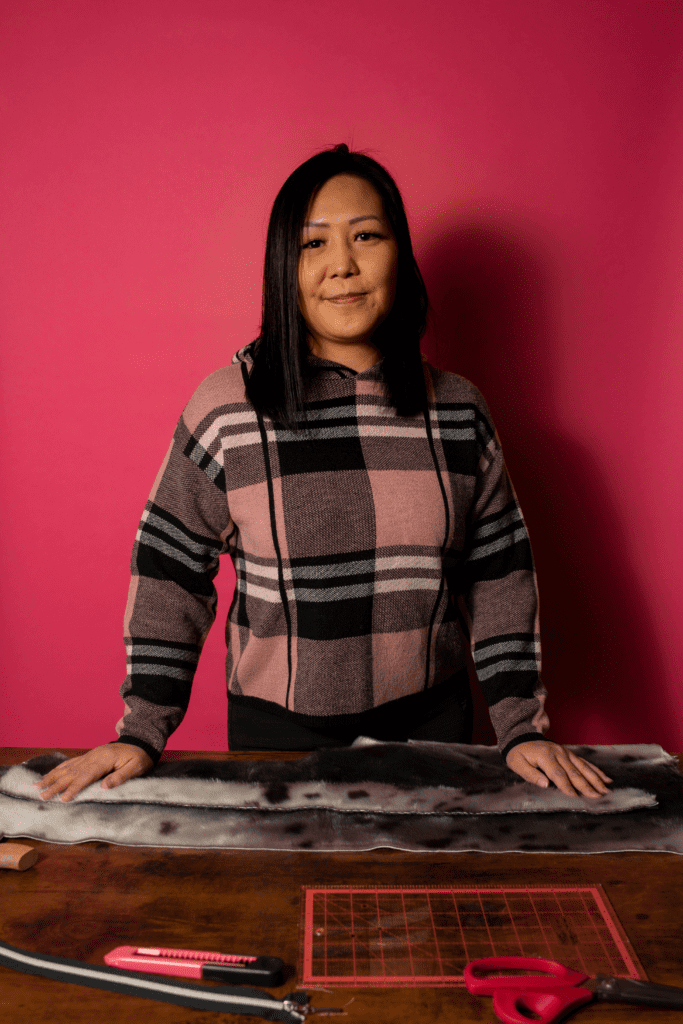 A woman stands with materials to sew a parka against a red background